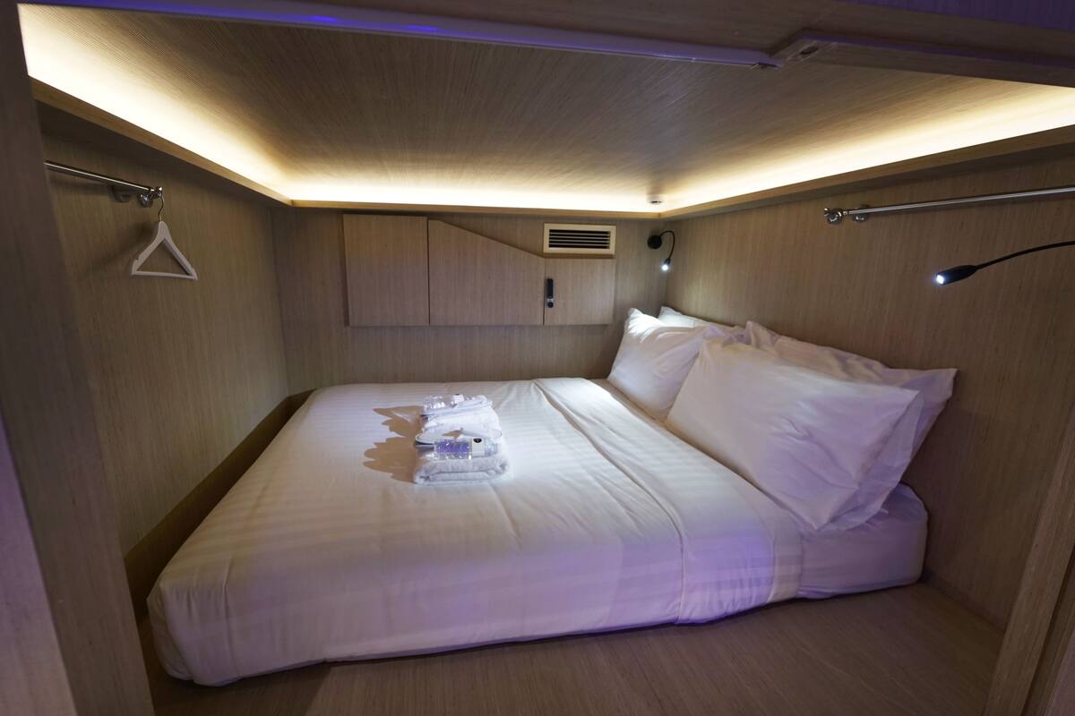 A neatly made bed with white linens and a set of towels, a wooden headboard, and a wall-mounted cabinet.