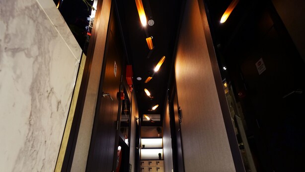 A corridor with marble walls, wooden paneling, and recessed lighting. - CUBE Boutique Capsule Hotel @ Kampong Glam (Singapore)