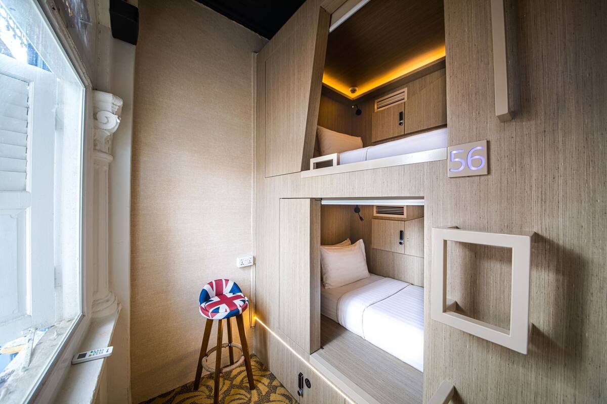 A compact, well-lit room with bunk beds, a small stool with a Union Jack cushion, and a number '56' sign on the wall.