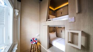 A compact, well-lit room with bunk beds, a small stool with a Union Jack cushion, and a number '56' sign on the wall.