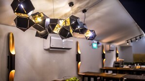 A restaurant interior with hexagonal pendant lights, wooden tables, and chairs. - CUBE Boutique Capsule Hotel @ Kampong Glam (Singapore)