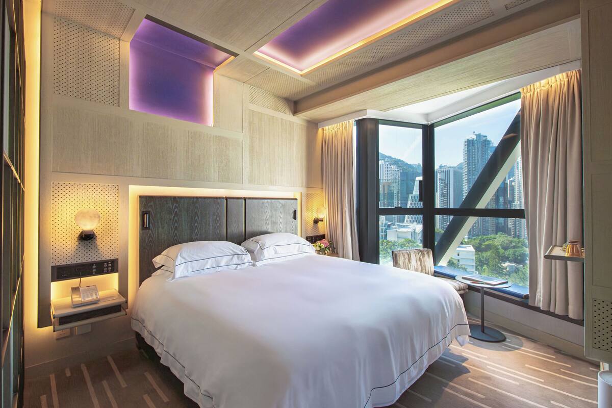 A modern hotel room with a large bed, city view, and contemporary design elements.