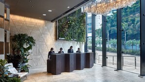 A reception area with a modern design, featuring a reception desk, seating area with plants, and large windows providing a view of the outdoors.