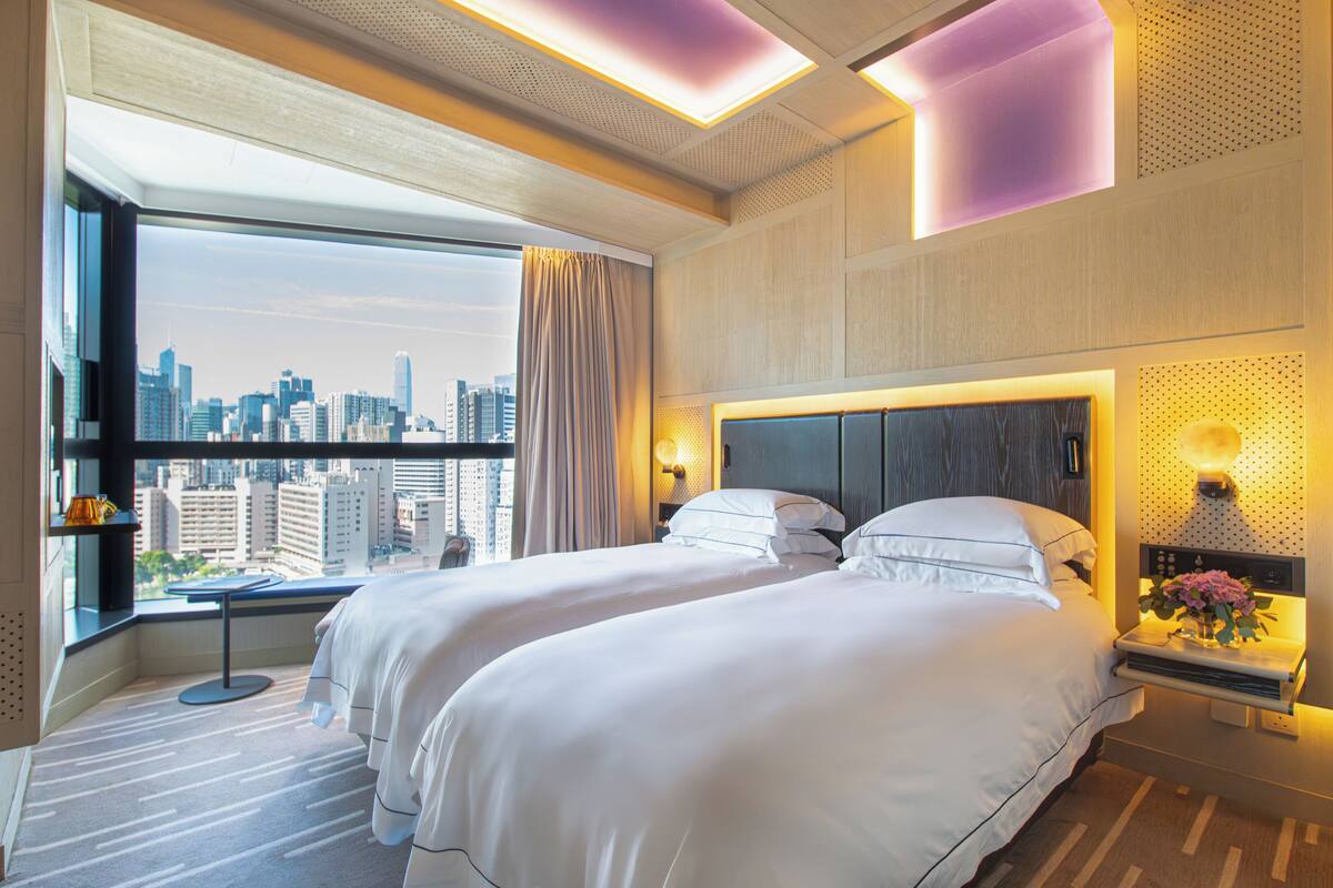 A hotel room with two beds, a city view, a large window, and a modern design.