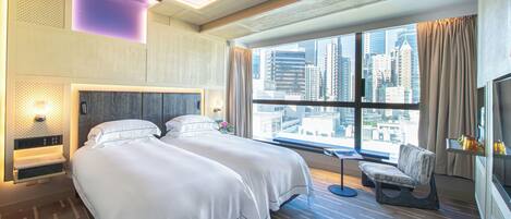 A modern hotel room with a large bed, a seating area, and a city view through large windows.