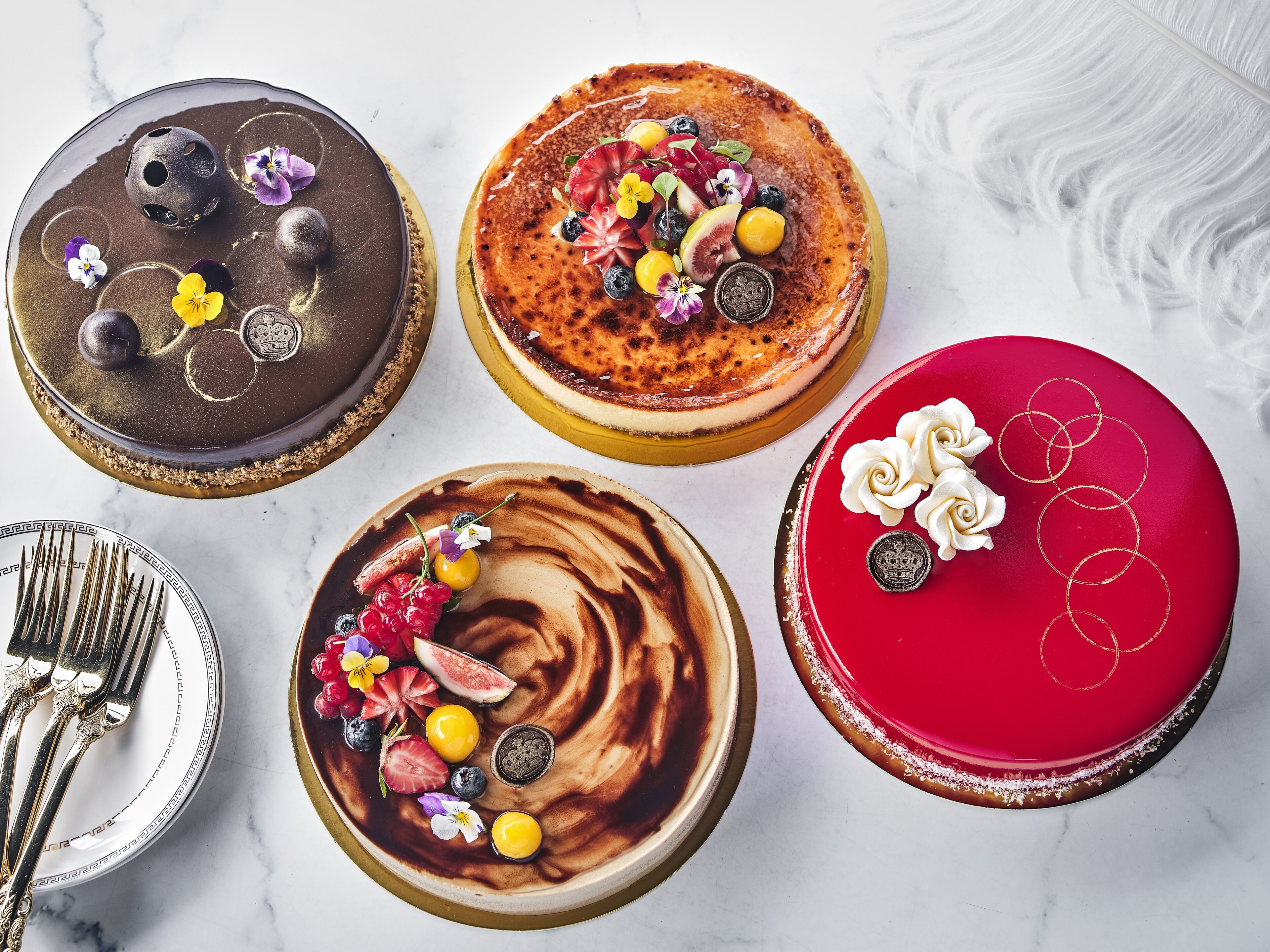 Five cakes with various toppings and designs on a marble surface.
