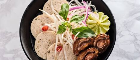 A bowl of food with sliced meat, noodles, and vegetables.