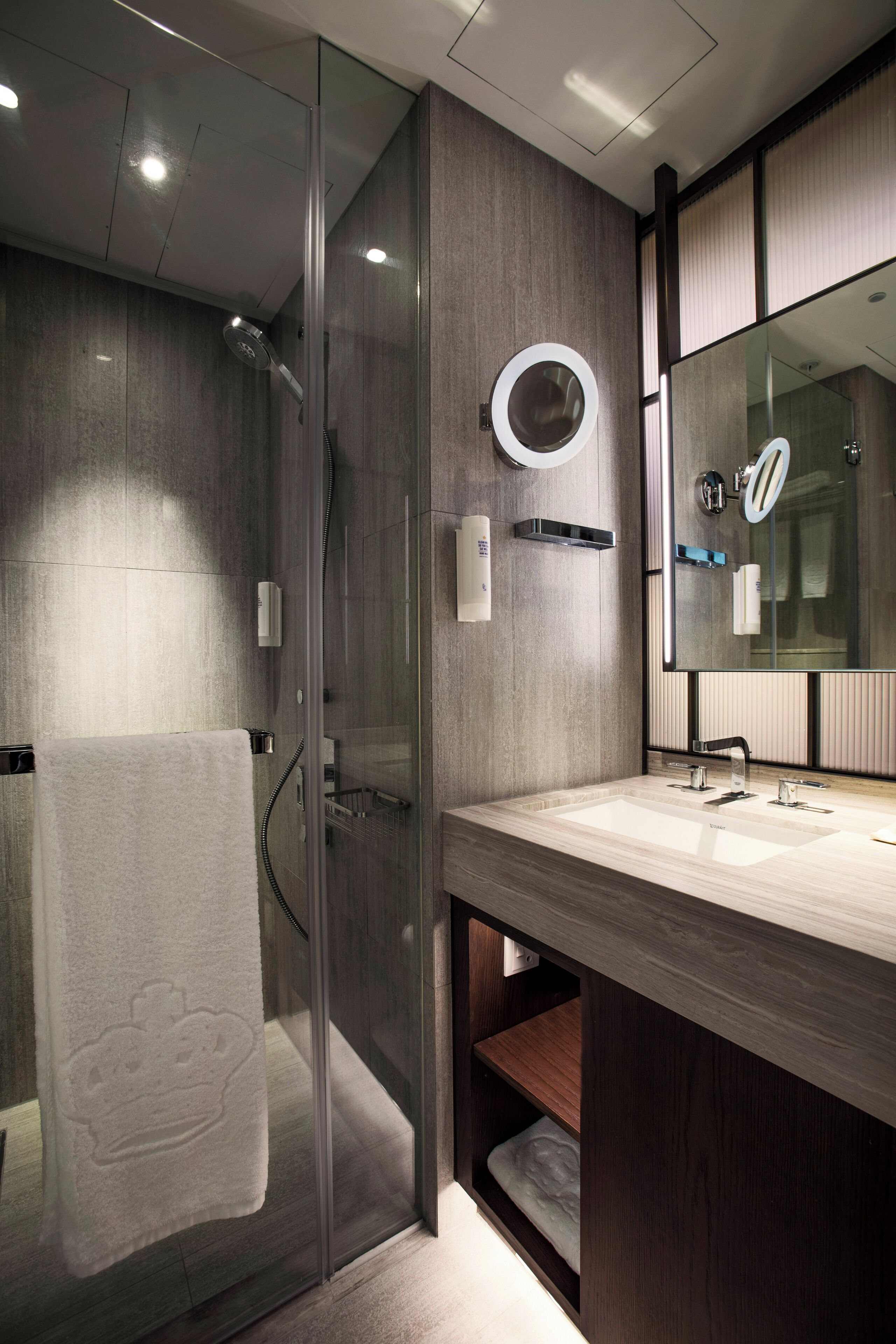 A modern bathroom with a glass-enclosed shower, a large mirror, and a wooden vanity with a towel rack.