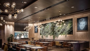 A modern restaurant interior with a bar area, seating arrangements, and a wall with greenery.