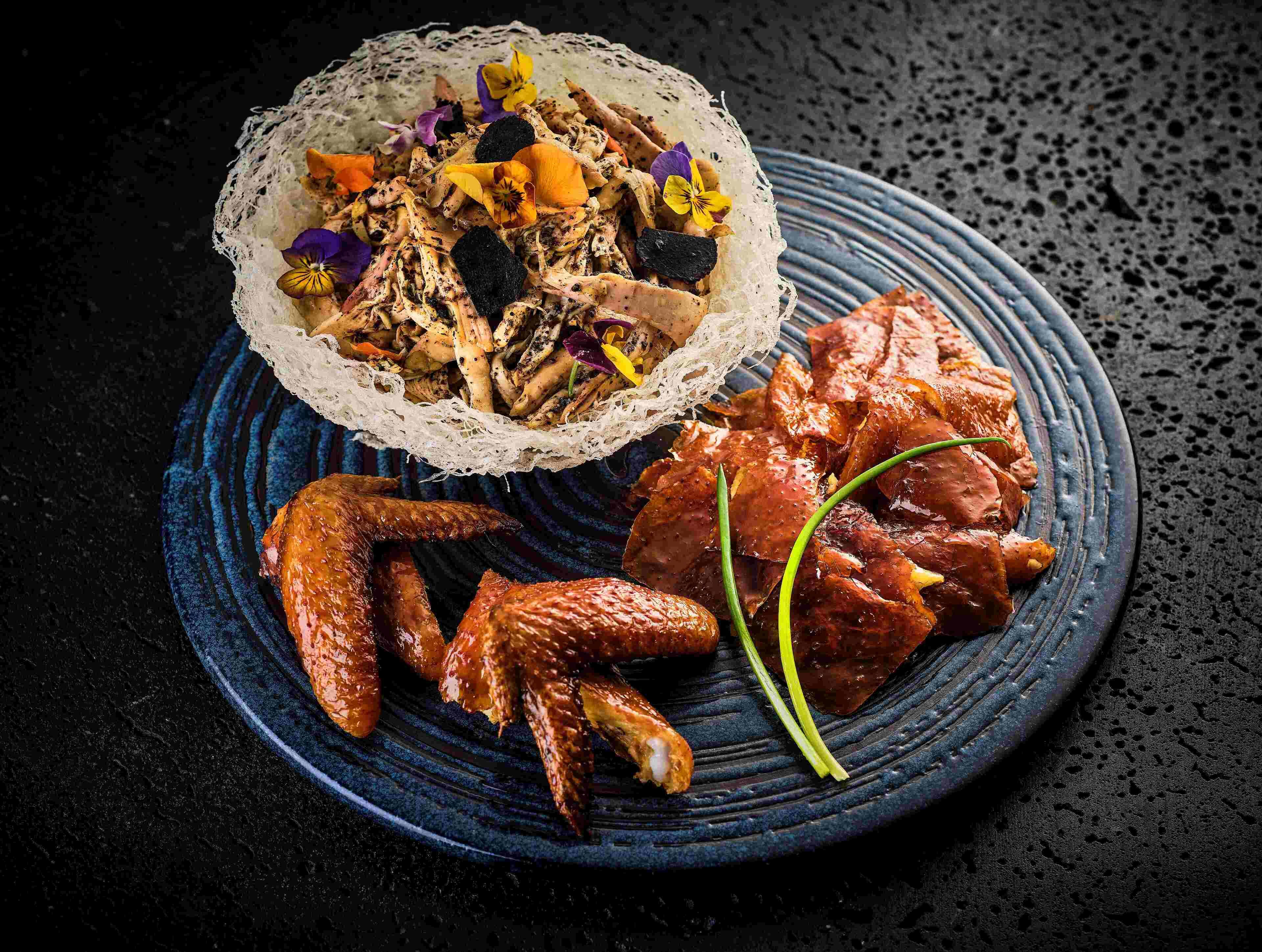 A plate with grilled chicken wings and a bowl of salad with various vegetables and herbs.