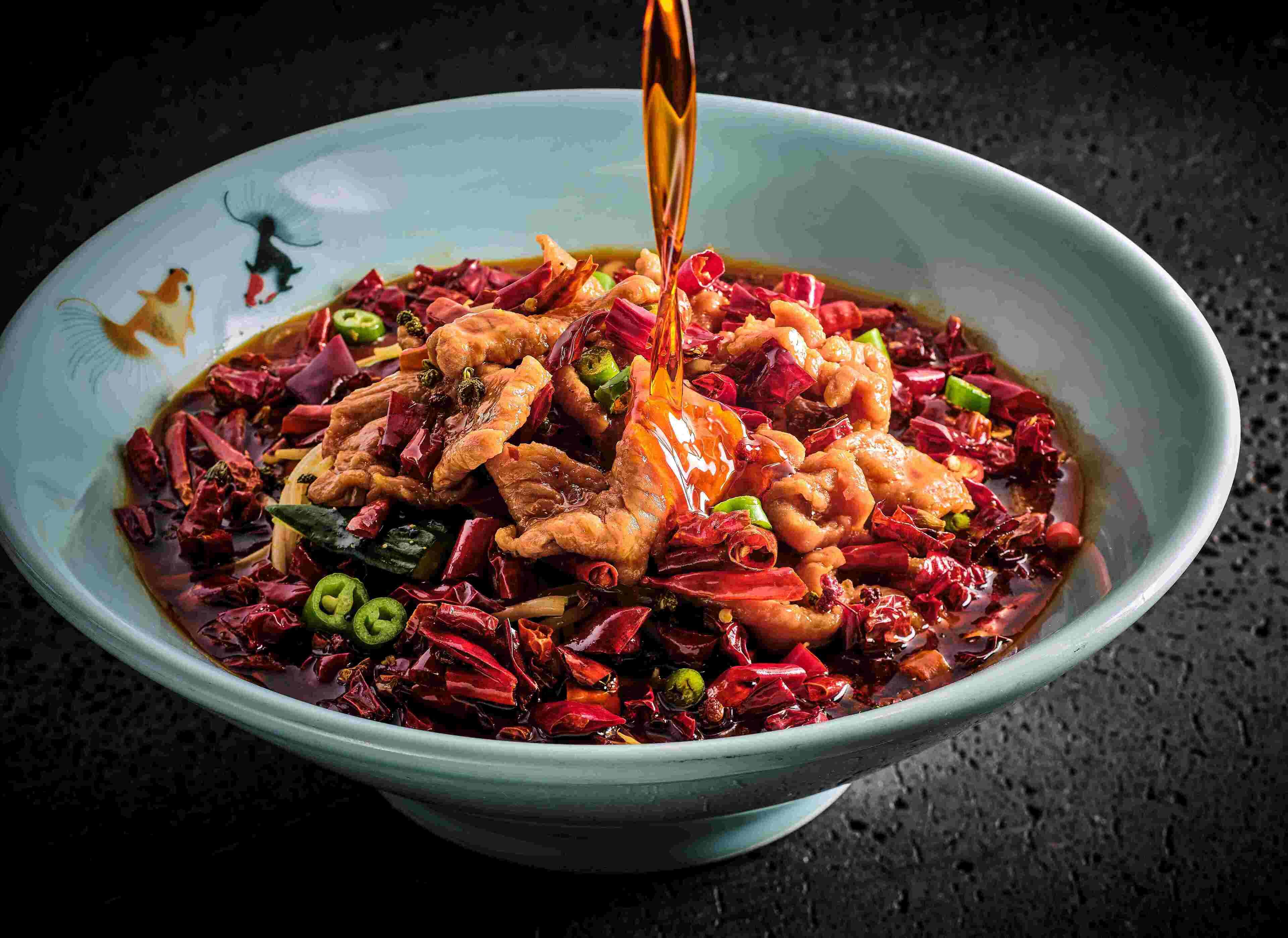 Un tazón de plato salteado picante con varios ingredientes y salsa vertiéndose sobre él.