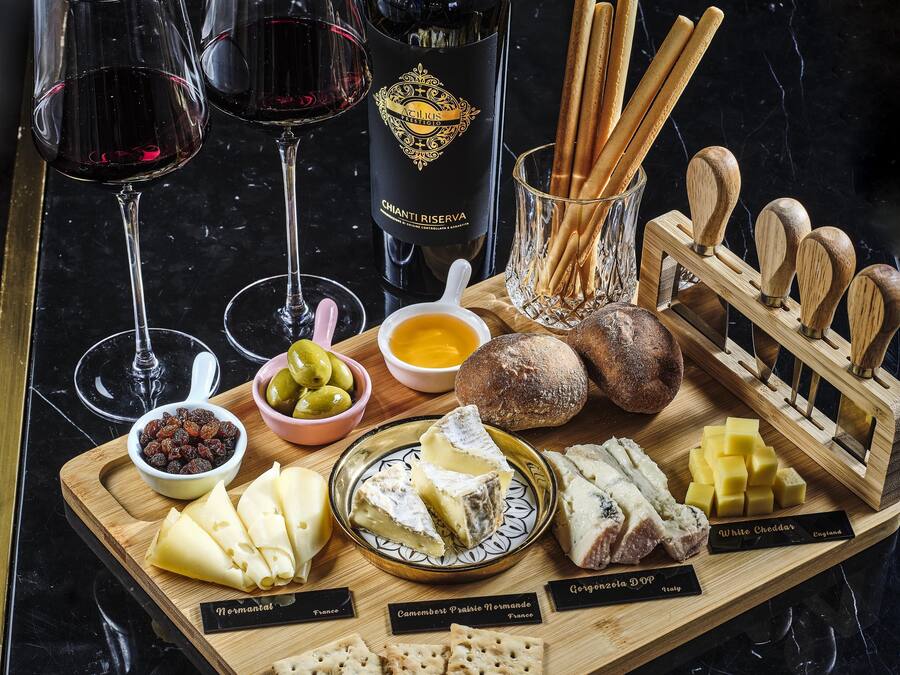A charcuterie board with various cheeses, crackers, olives, and breadsticks.
