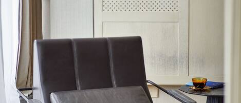 A modern chair with a cushioned seat and backrest, positioned in a room with wooden flooring and a window with curtains.