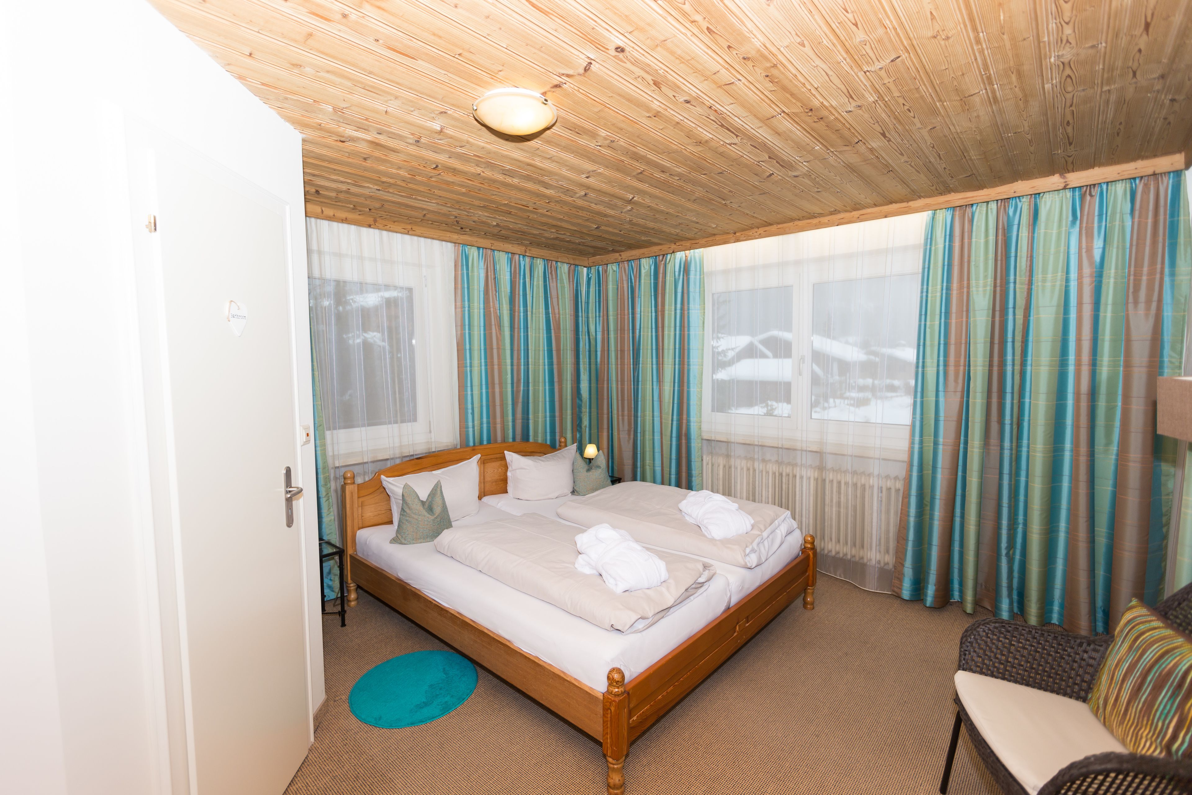 Una habitación de hotel con techo de madera, una cama con dos almohadas, una mesita de noche y una silla.