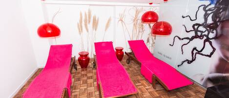 Una habitación con tres mesas de masaje de madera cubiertas con toallas rosas, lámparas esféricas rojas y plantas decorativas.