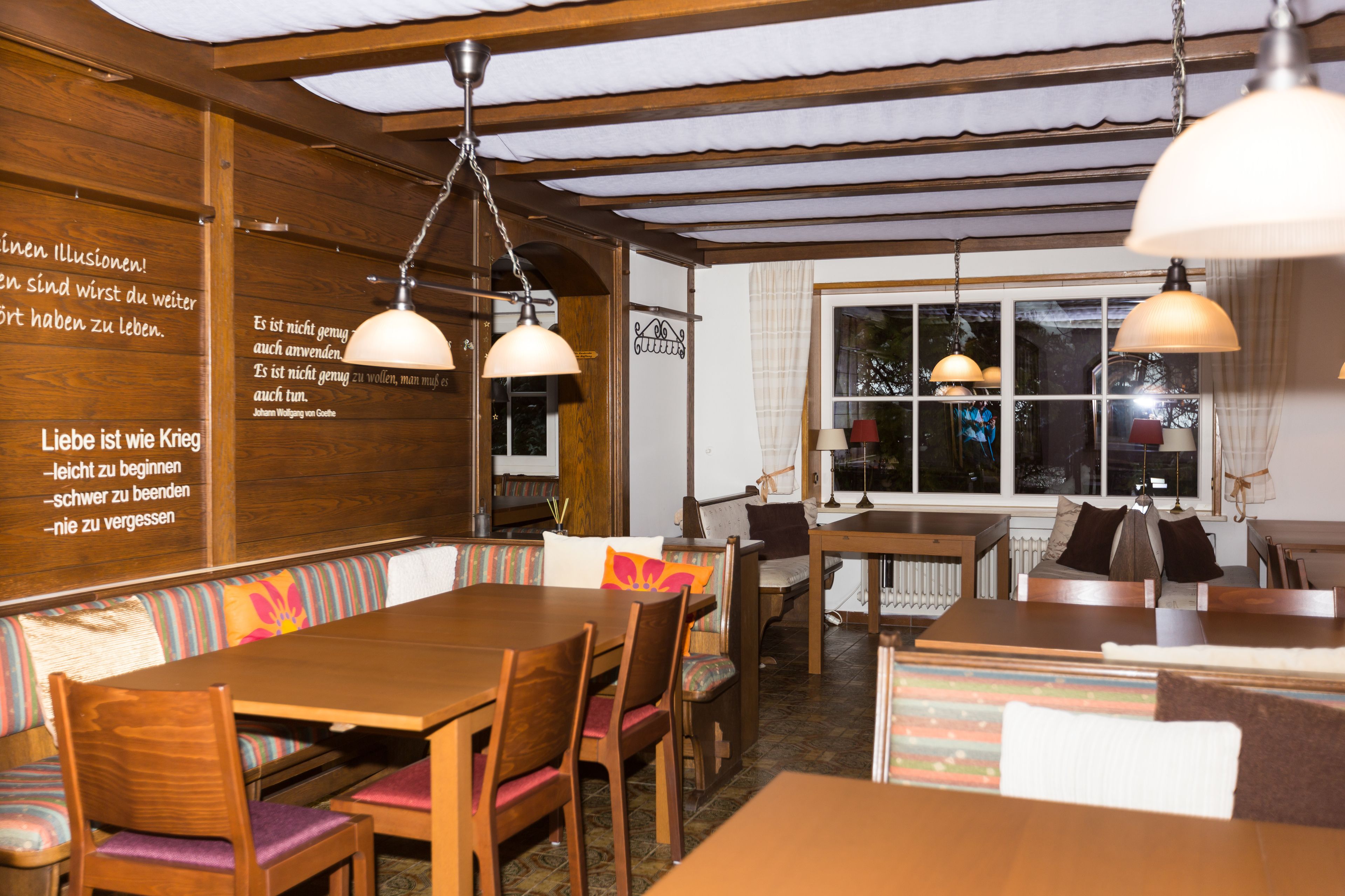Un restaurante acogedor con muebles de madera, una larga mesa común y lámparas colgantes.