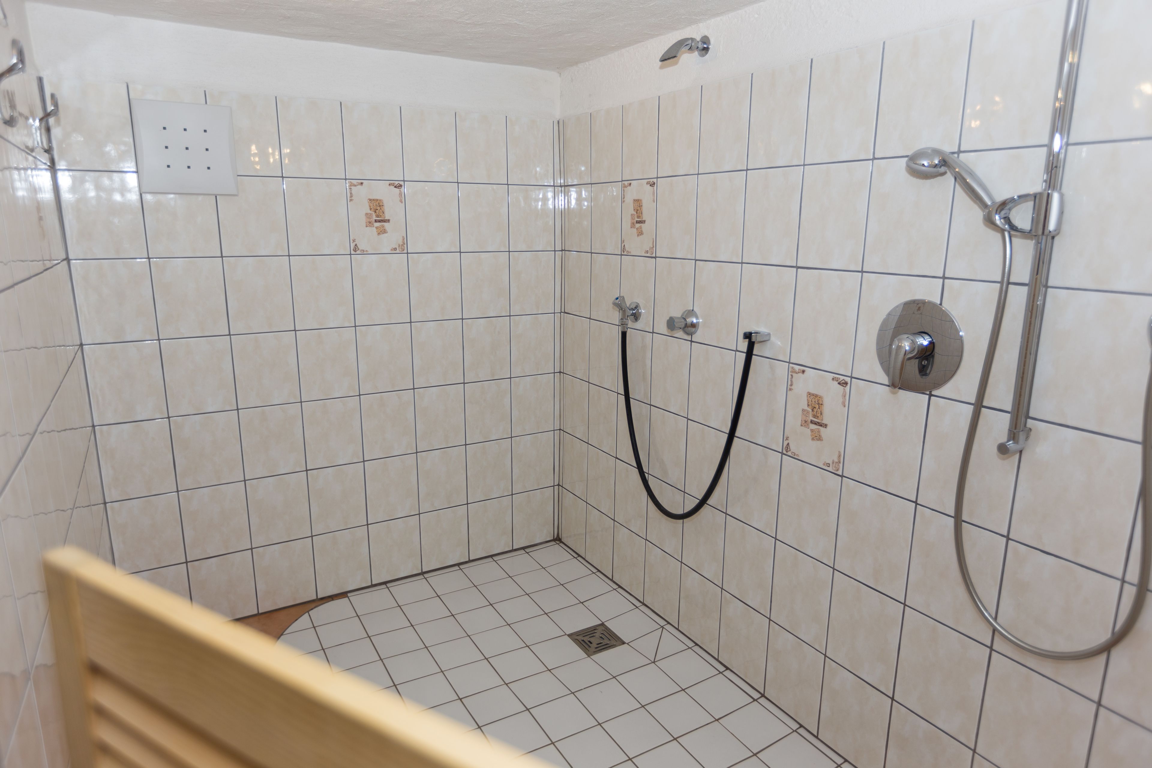 Un pequeño box de ducha con azulejos, con ducha de mano y manguera.