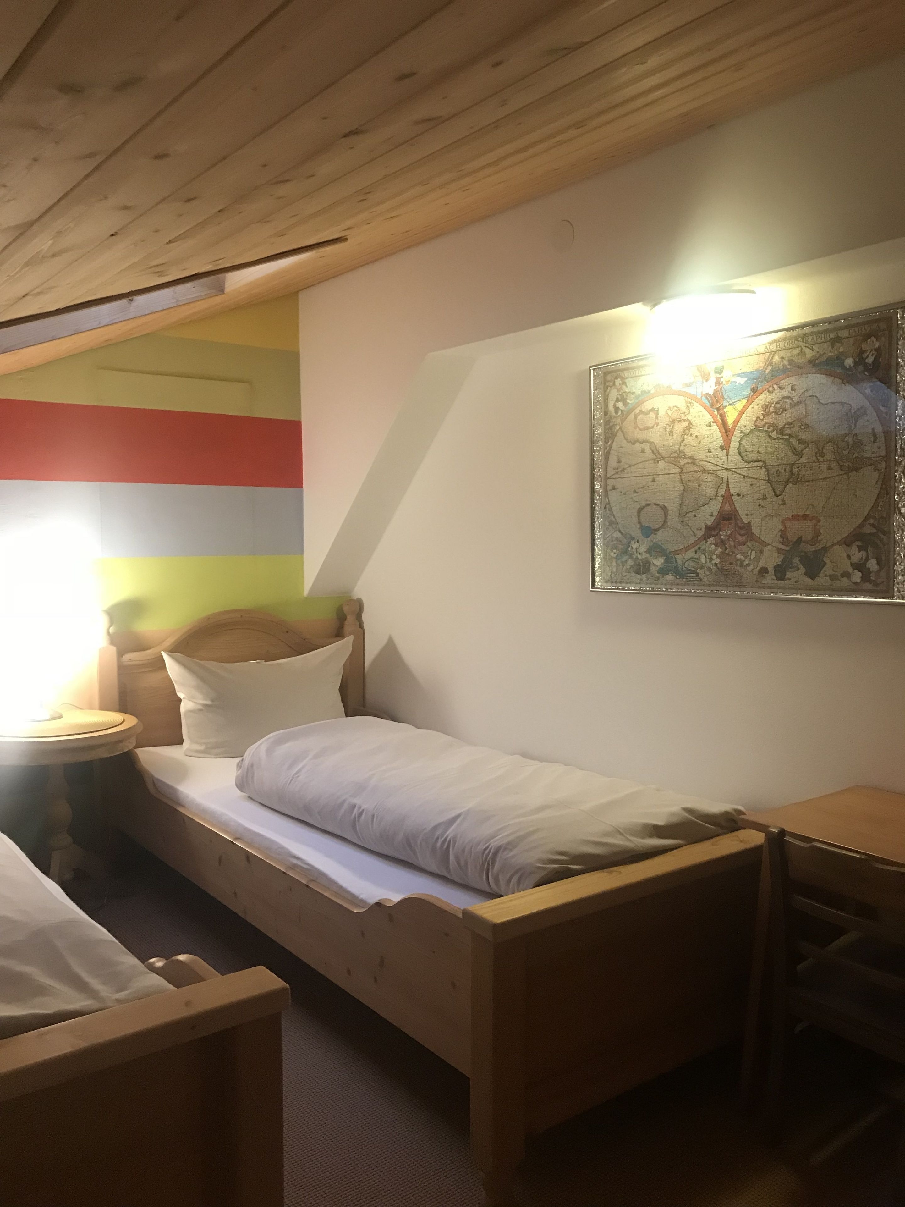 A single bed with a wooden headboard, a bedside table with a lamp, and a wall-mounted map.