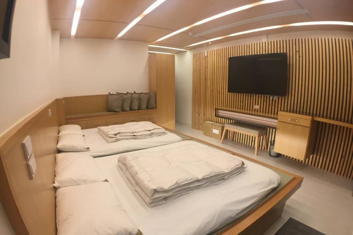 A modern hotel room with a large bed, a TV mounted on a wooden panel wall, and a piano.