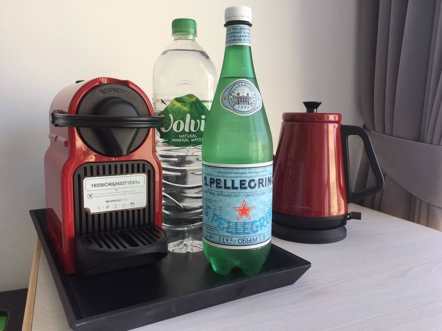 A coffee maker, a bottle of sparkling mineral water, and a kettle on a table.