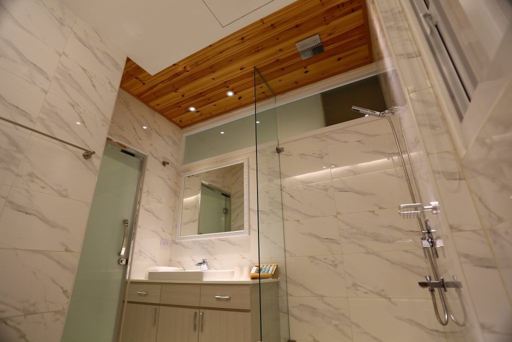 Un baño moderno con techo de madera, paredes de mármol, cabina de ducha de vidrio y tocador con espejo.