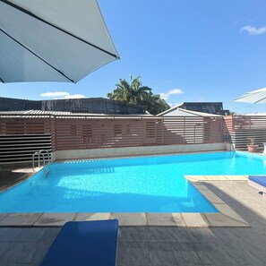 Une piscine à l’eau d’un bleu cristallin, entourée d’une clôture en bois et surmontée d’un auvent blanc.