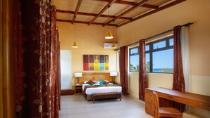 Quarto com cama, mesas de cabeceira, escrivaninha e vista para o mar.