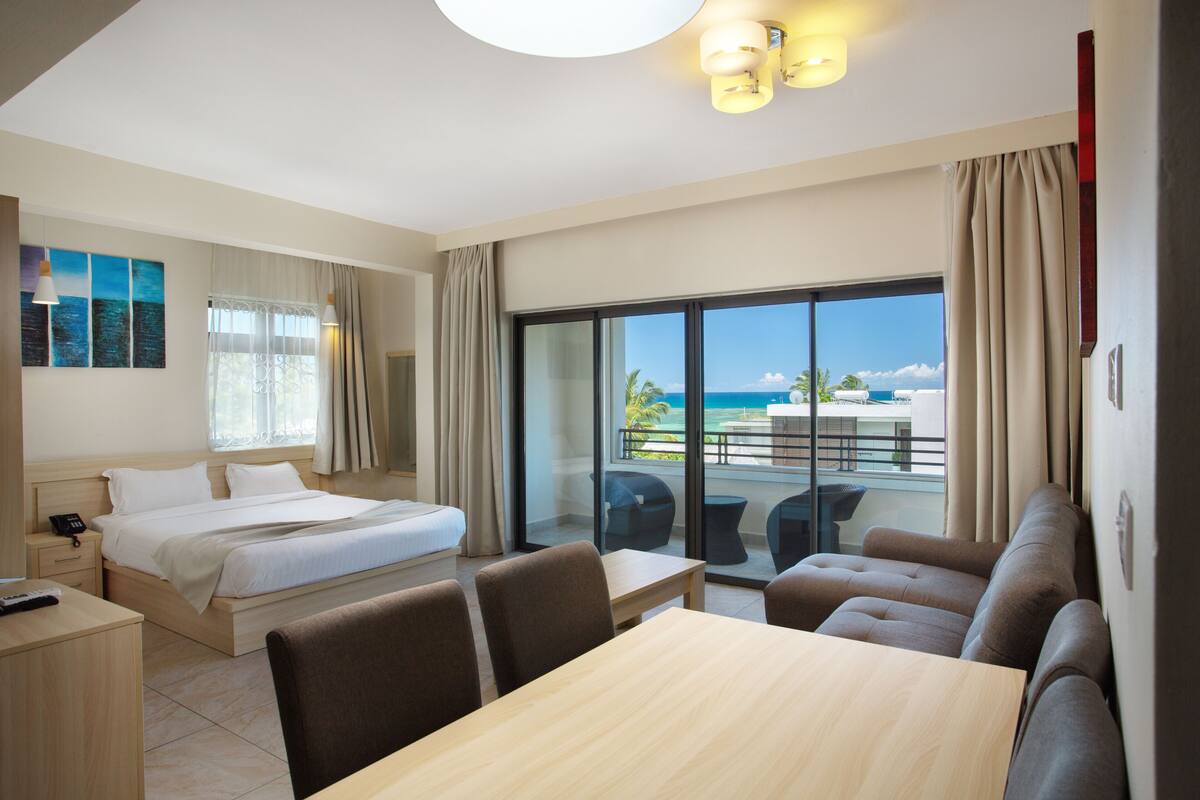 Une chambre d’hôtel avec un lit, une table à manger et un balcon donnant sur l’océan.