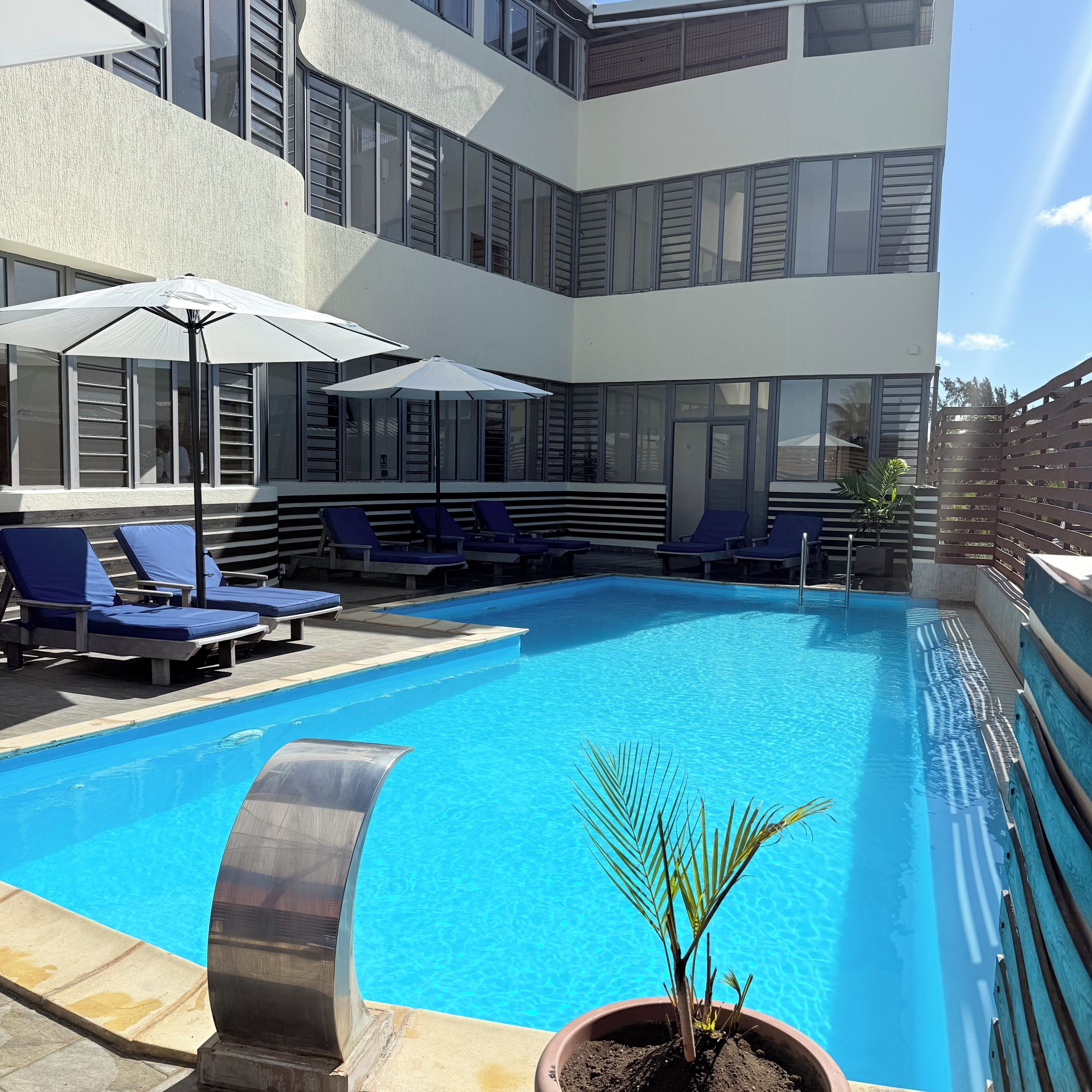 A modern building with a swimming pool, sun loungers, and umbrellas.