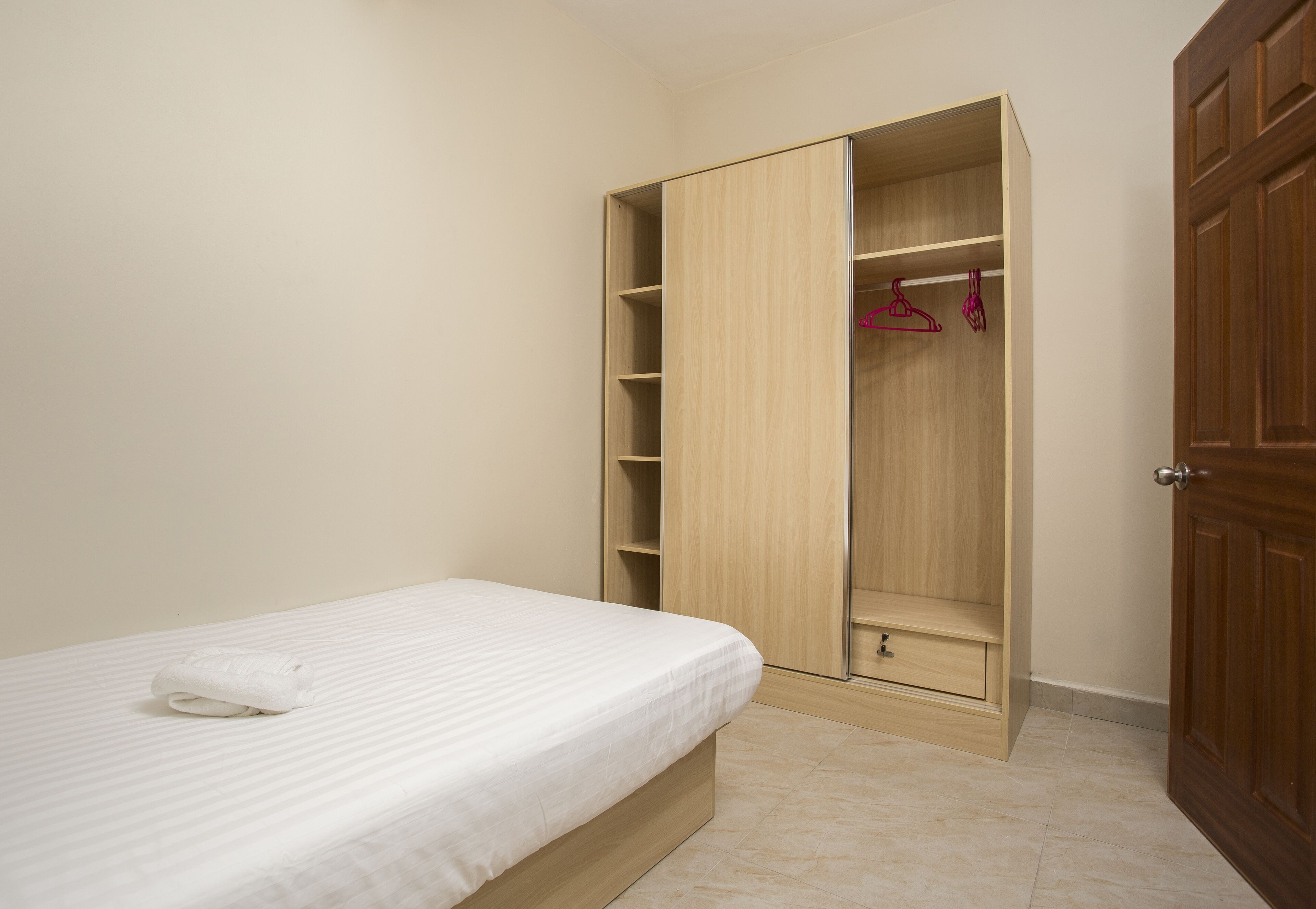 Un dormitorio con una cama, un armario de madera con varios estantes y una puerta.