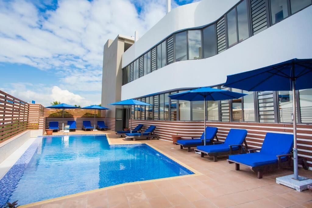 Una piscina interior con sillones azules y sombrillas, rodeada por un edificio moderno con grandes ventanales.