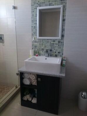 A bathroom with a white sink, a mirror, and a tiled backsplash. There are towels stored in a cabinet below the sink. - Lifestyle Apartments (Gaborone)