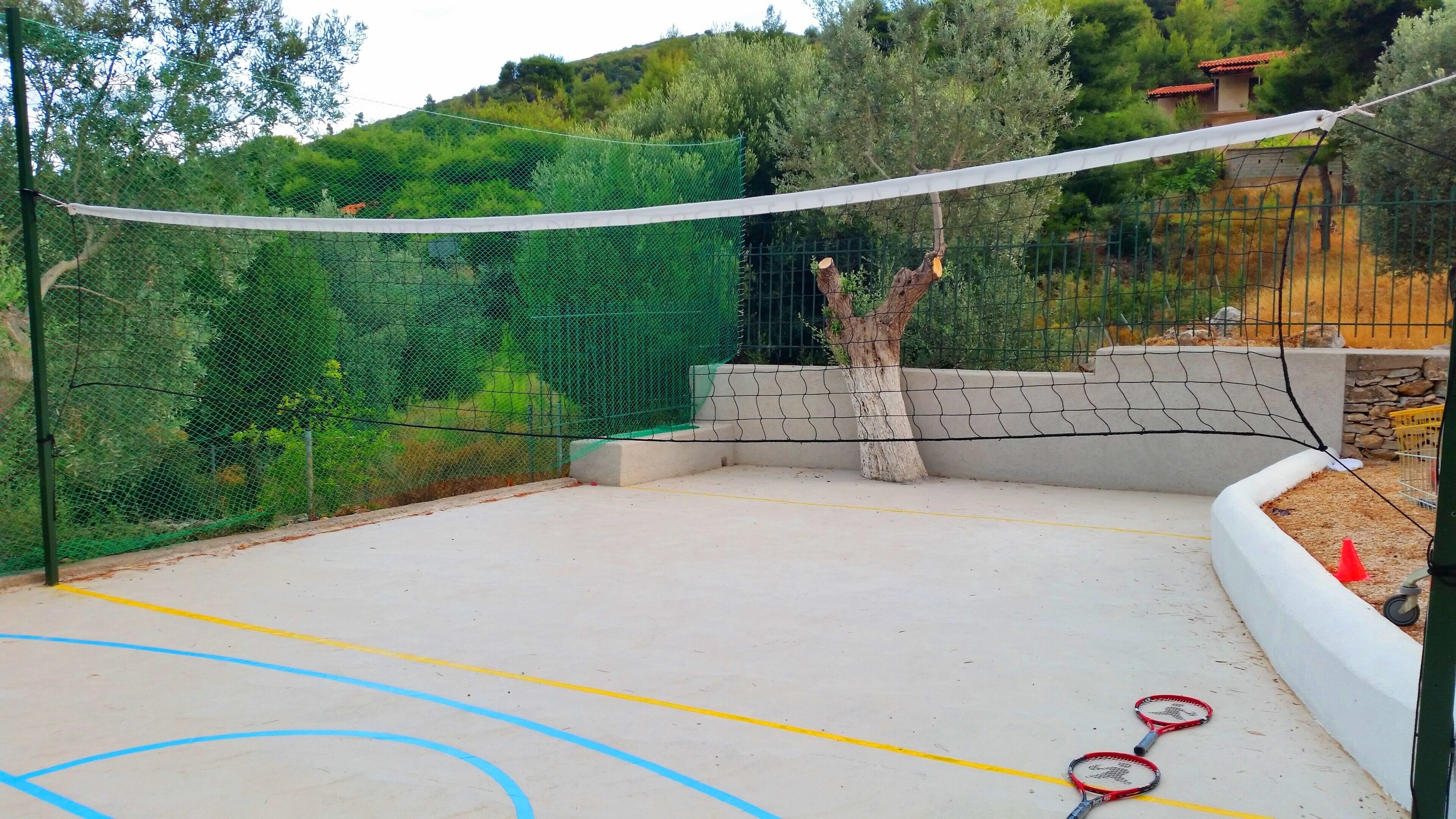 Ein Tennisplatz im Freien mit Netz, umgeben von einem grünen Zaun und Bäumen.