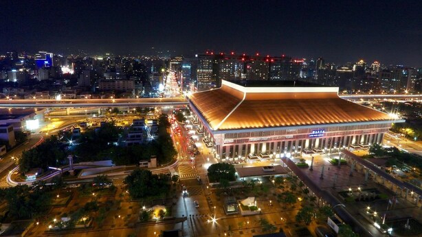 A large, modern building with a prominent roof and multiple columns, surrounded by well-lit streets and other buildings. - Sky19 Hotel (Taipei)