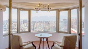 A corner room with a panoramic city view, a round table, two chairs, and a chandelier. - Sky19 Hotel (Taipei)