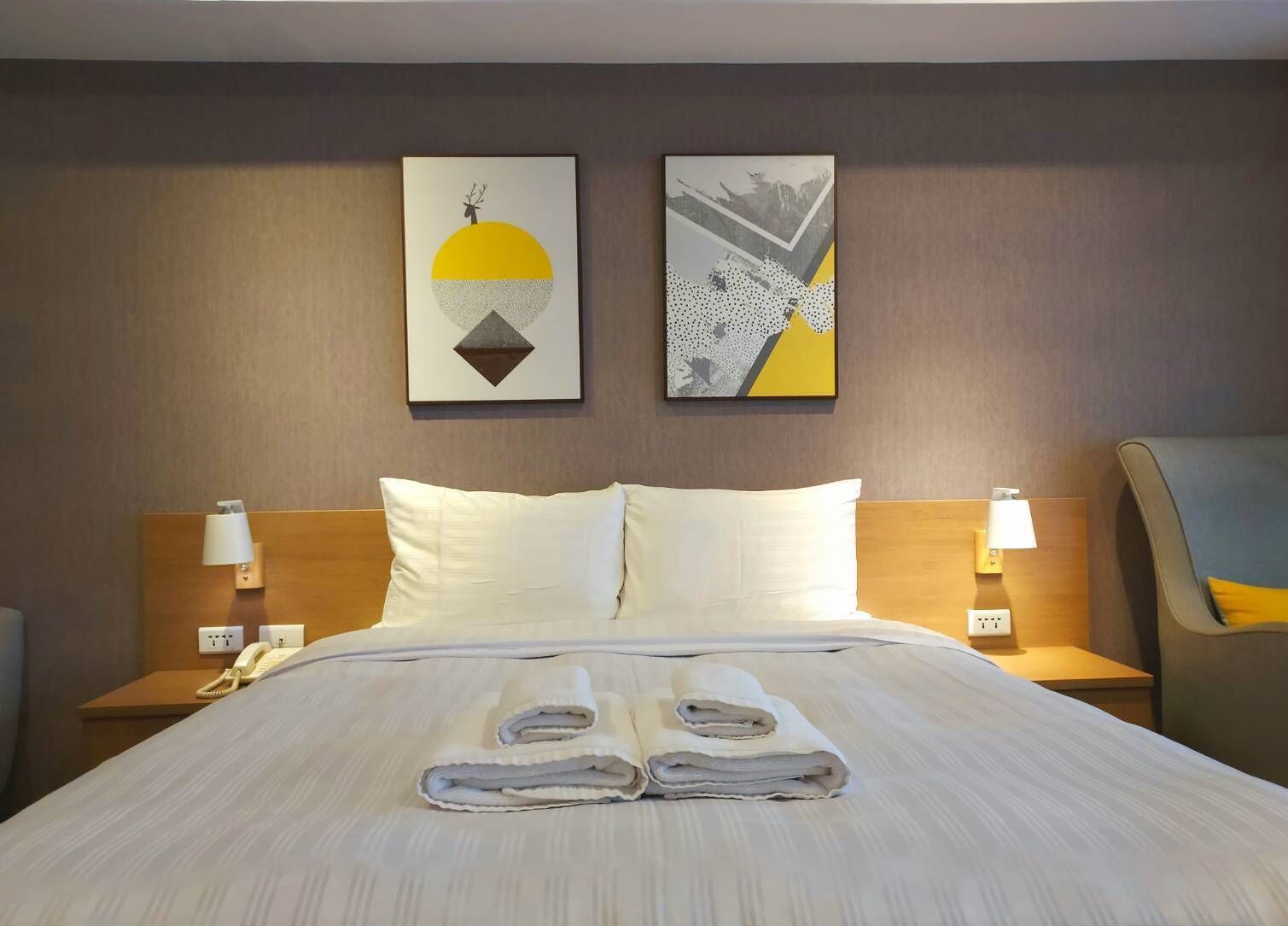 Ein Hotelzimmer mit einem ordentlich bezogenem Bett, zwei Nachttischlampen, einem Telefon und zwei abstrakten Bildern an der Wand.