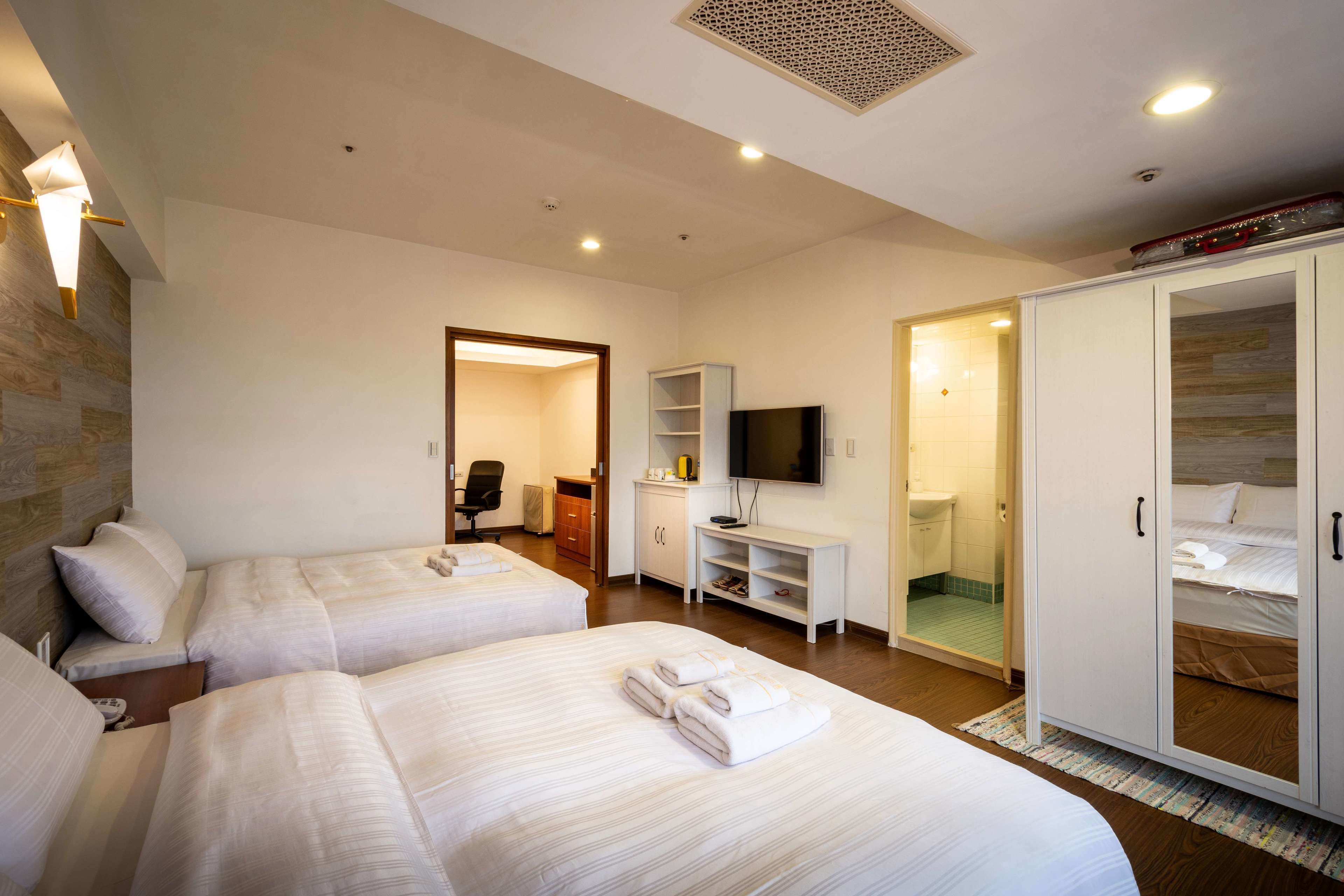 A hotel room with two beds, a TV, a wardrobe, and a bathroom.