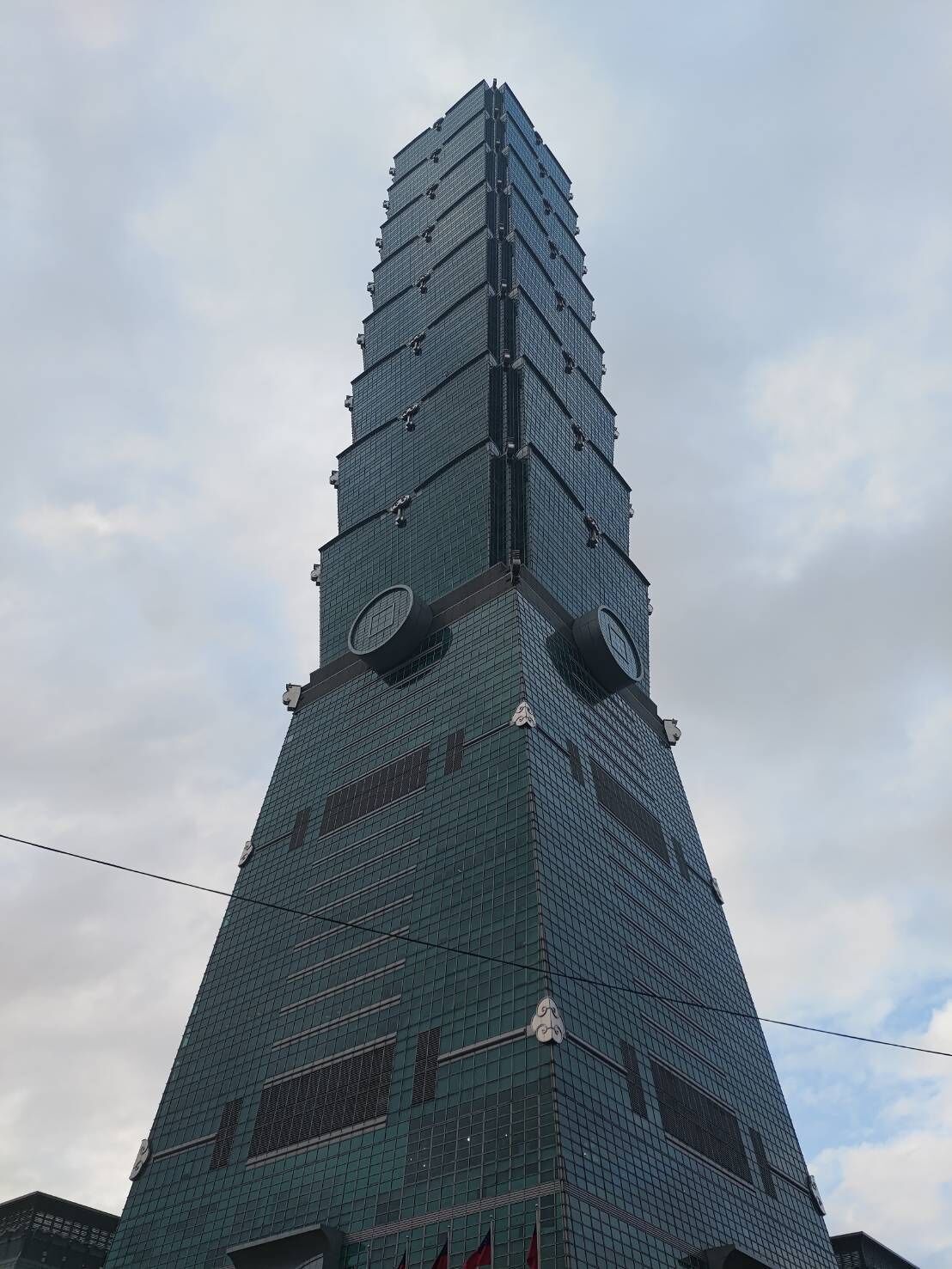 En høj, moderne skyskraber med et markant, trappetrin-formet design og et ur øverst.