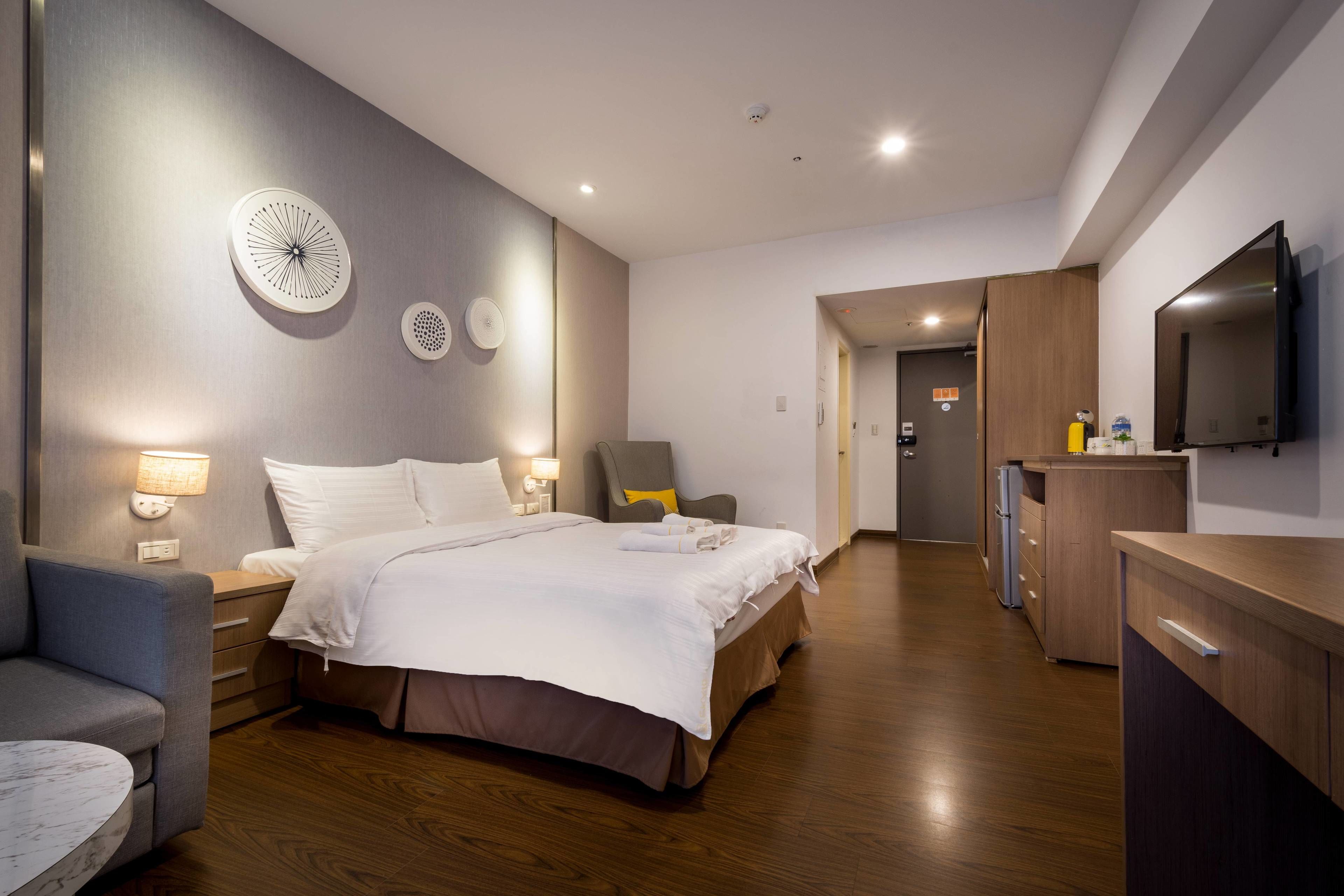 Ein modernes Hotelzimmer mit einem großen Bett, Nachttischen, einem Schreibtisch und einem Flachbildfernseher.