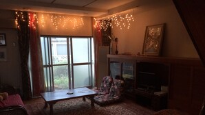 A cozy living room with a sofa, a coffee table, and a TV. There are curtains and a window with a view outside.