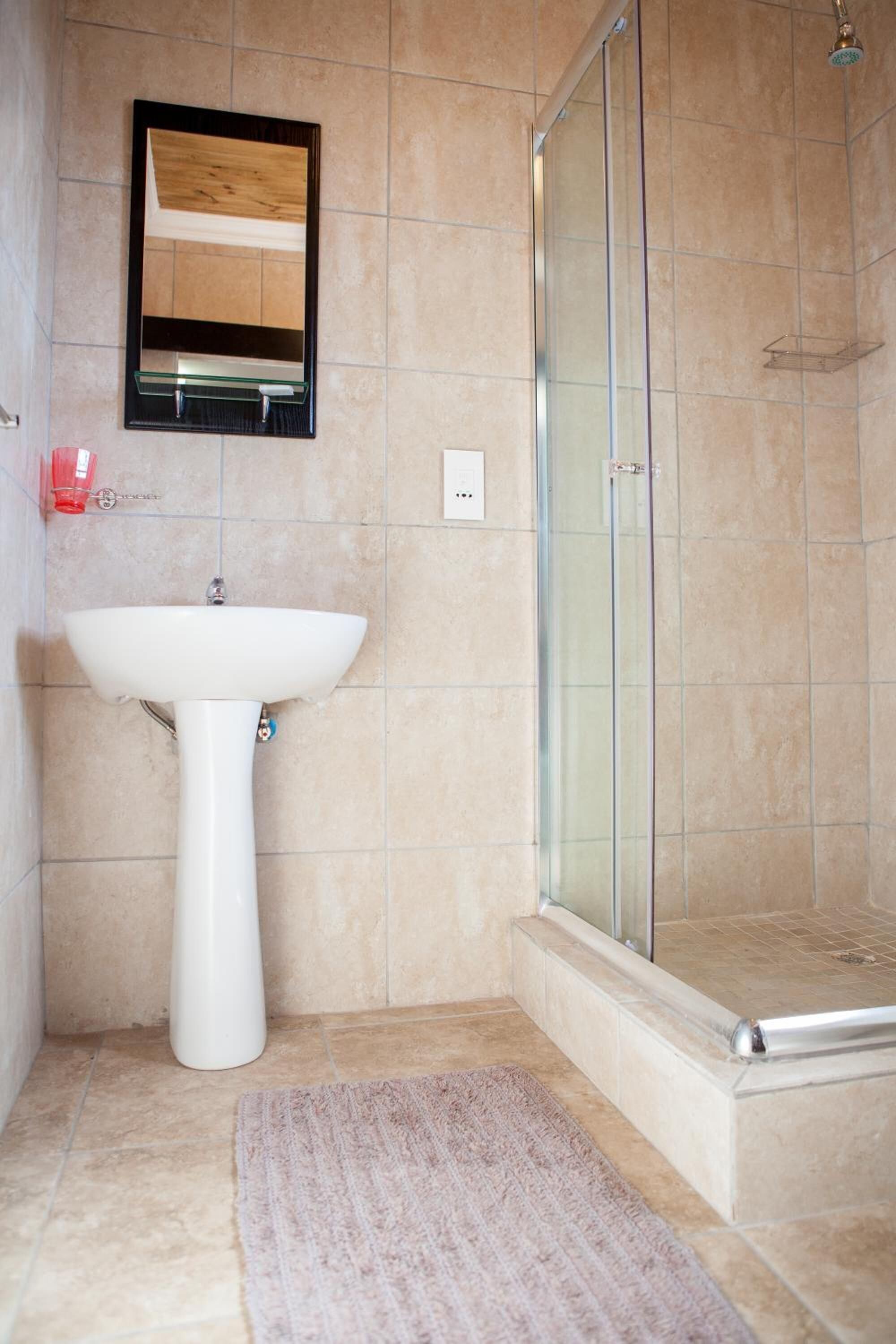 A bathroom with a white pedestal sink, a glass shower enclosure, and a beige tiled floor.