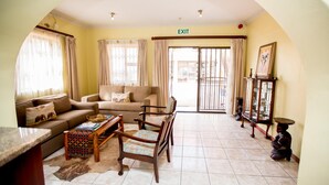 A spacious living room with a sofa, chairs, a coffee table, and a dining table. An exit sign is visible on the wall. - Oria Guesthouse (Cape Town)