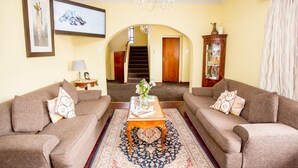 A living room with two sofas, a coffee table, a chandelier, a staircase, and a cabinet. - Oria Guesthouse (Cape Town)
