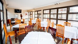 A dining area with tables and chairs, a television, and a fire extinguisher. - Oria Guesthouse (Cape Town)