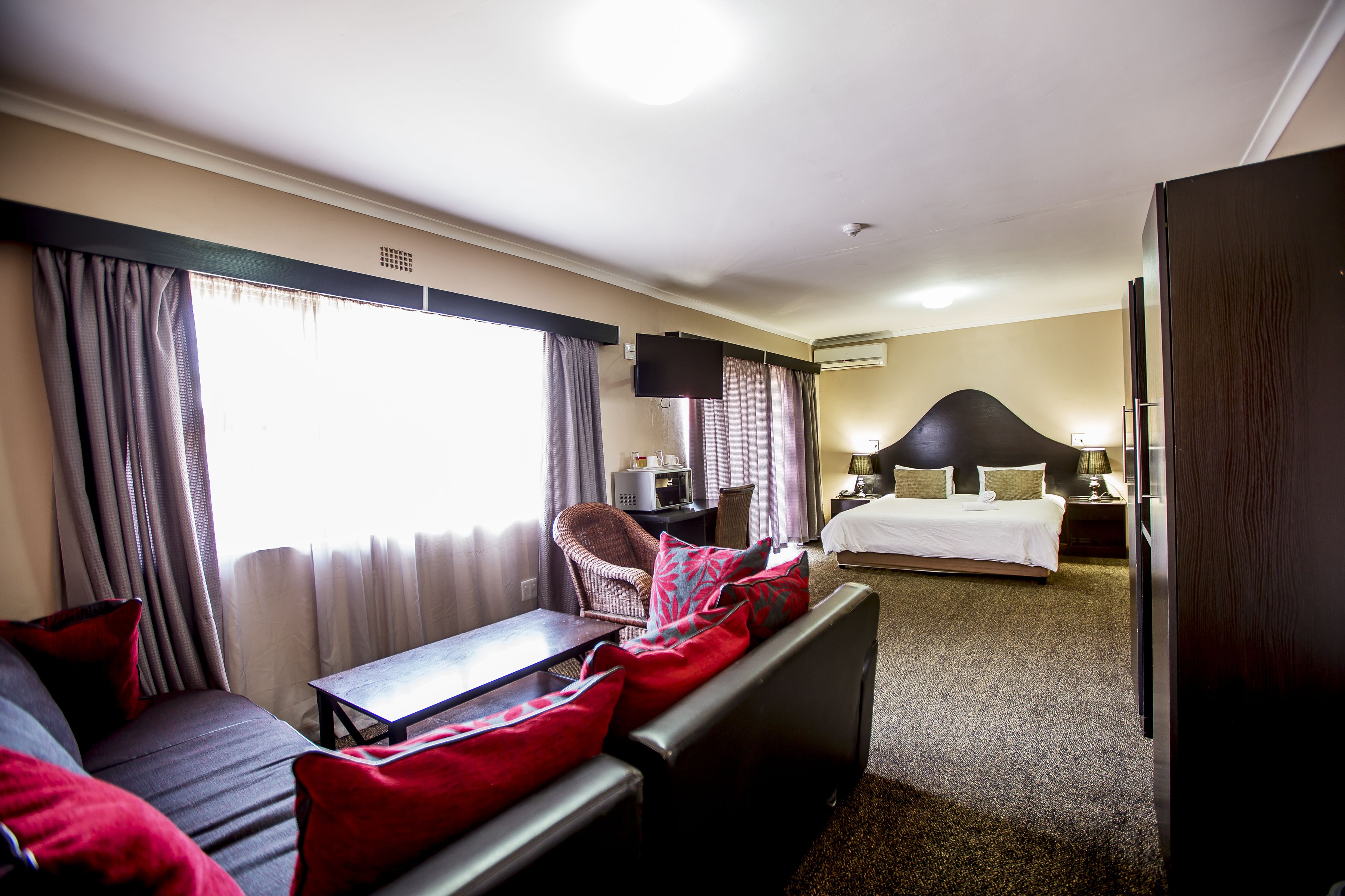 A hotel room with a sofa, a small table, a bed, a TV, and a nightstand.