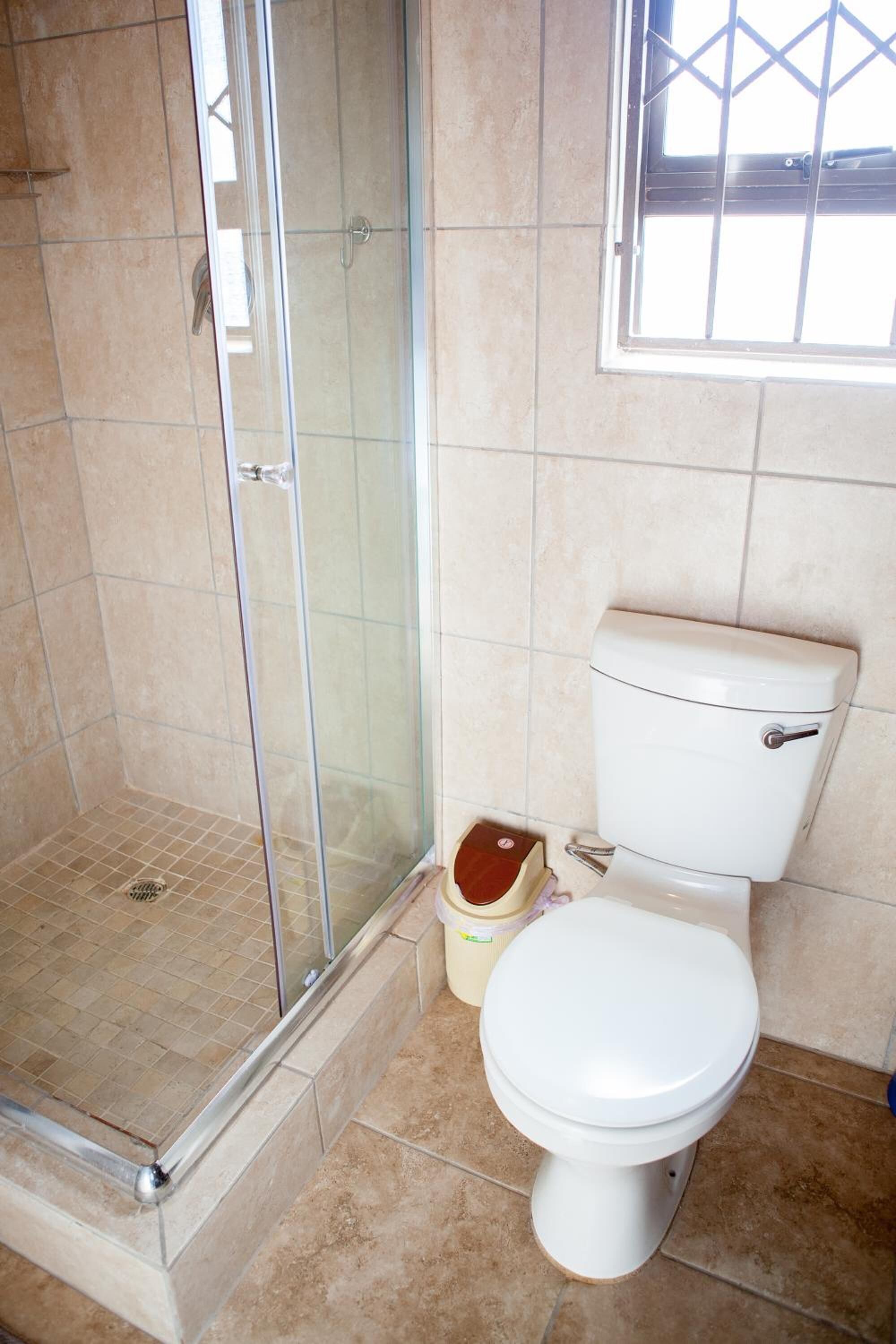 A bathroom with a glass-enclosed shower, a toilet, and a window.