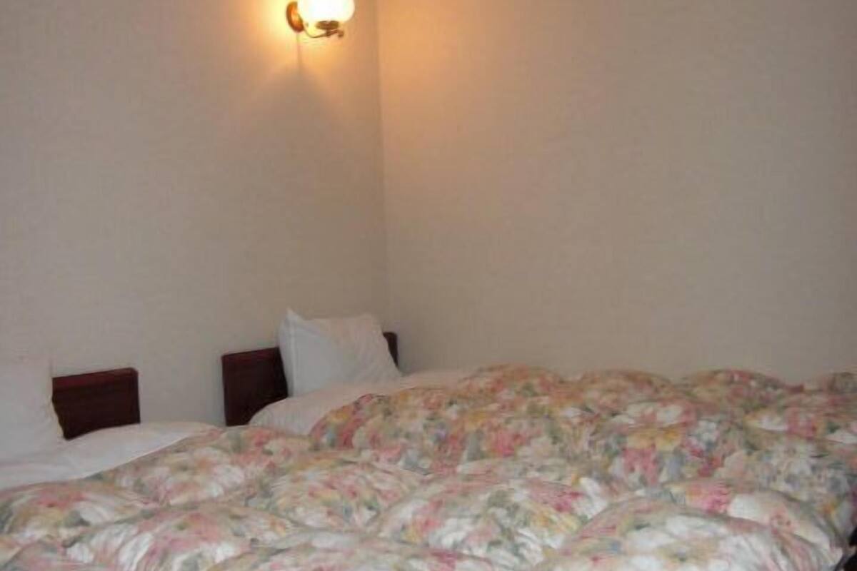 A bedroom with a floral-patterned bedspread, a single bed, and a wall-mounted light fixture.