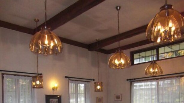 Un comedor con mesas y sillas de madera, iluminación colgante y amplios ventanales con cortinas.