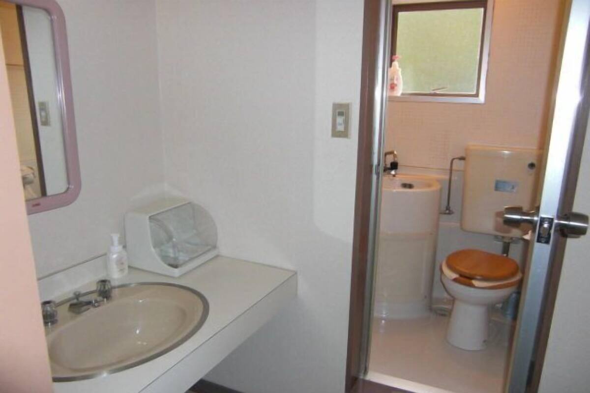 A bathroom with a sink, mirror, toilet, and a window.