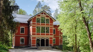 A two-story red building with a symmetrical facade, large windows, and a central entrance with steps. - Villa Santa Hotel (Cesis)
